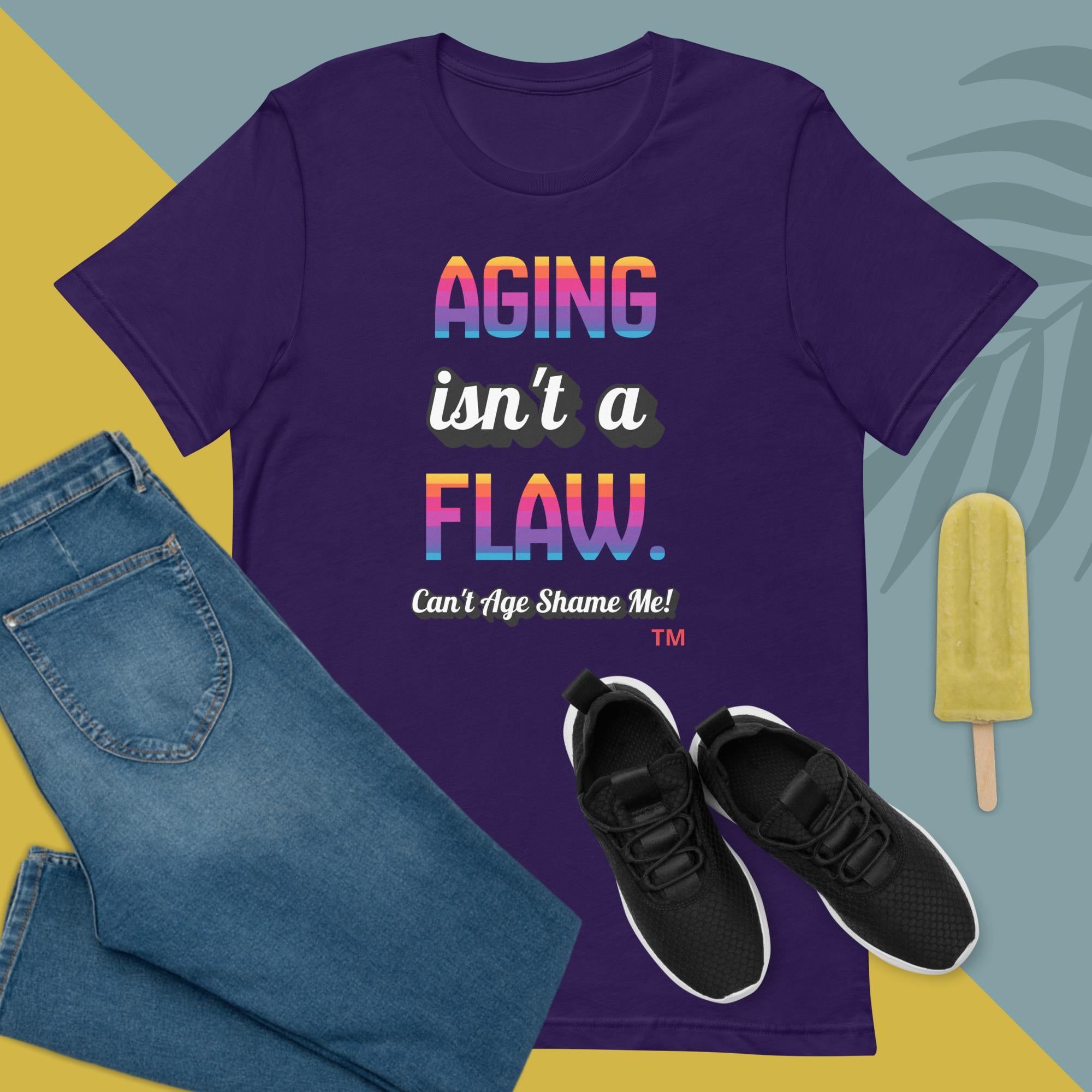Purple t-shirt with 'Aging isn't a flaw' text, paired with jeans and sneakers on a colorful background.