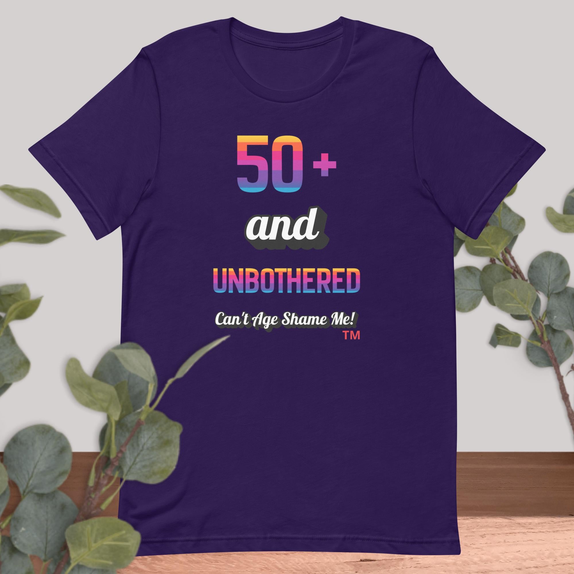 Purple t-shirt with colorful text design on a light gray background with green leaves.