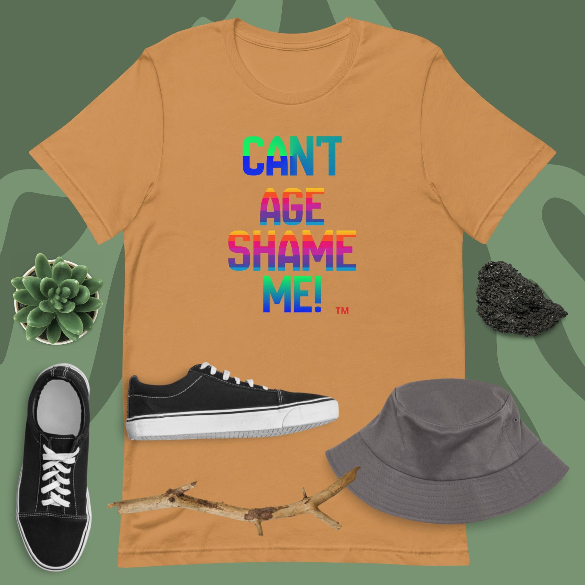 Orange t-shirt with colorful text, black sneakers, gray bucket hat, and branch on a green background