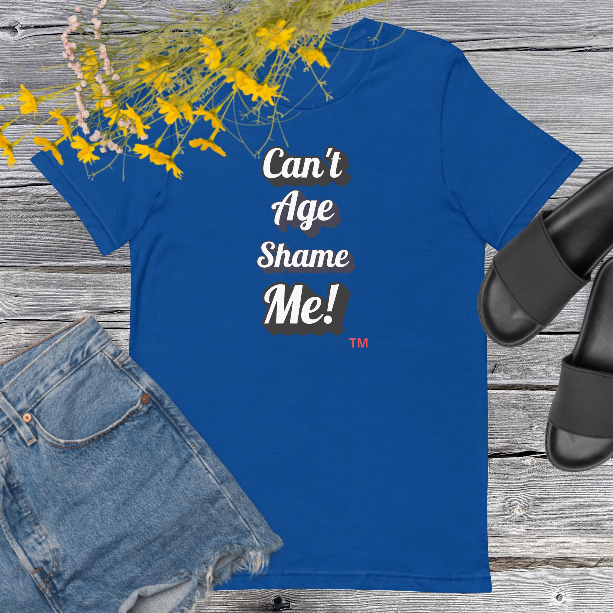 Blue t-shirt with 'Can't Age Shame Me!' text on a wooden surface with denim shorts and sandals.