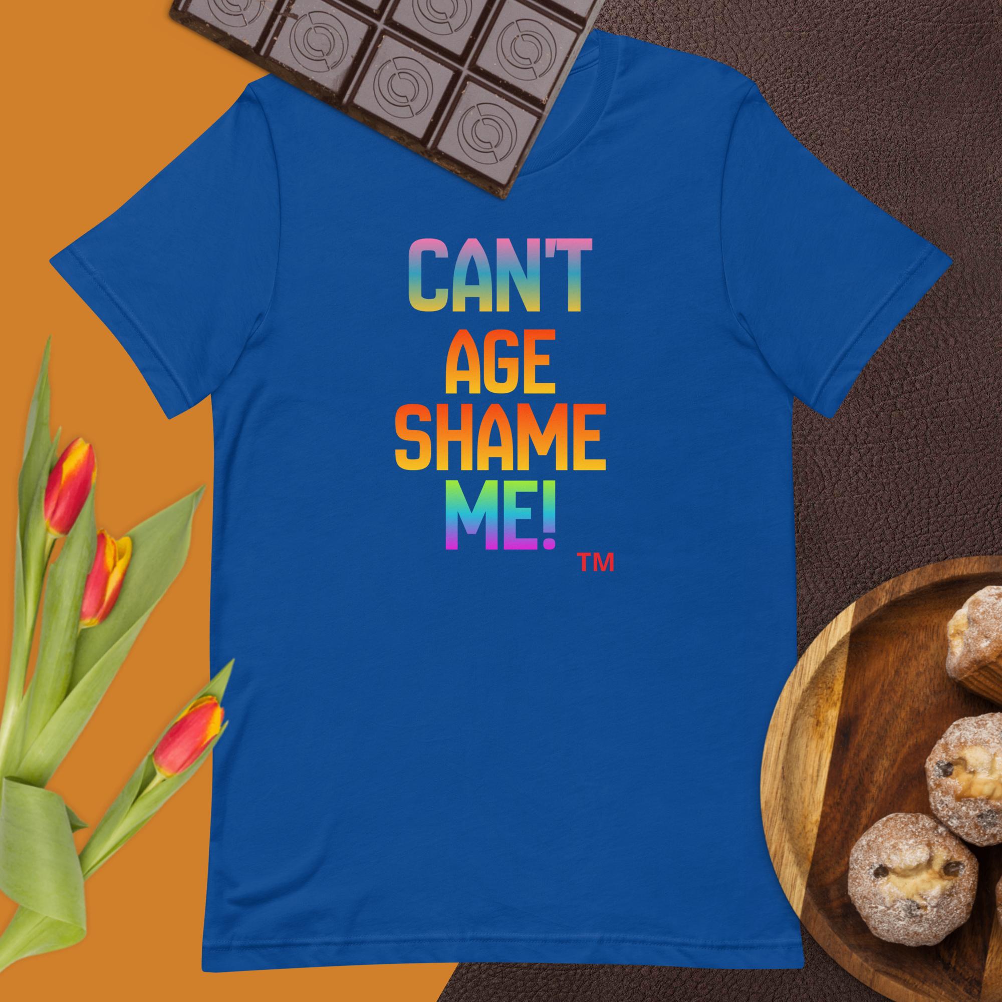 Blue t-shirt with colorful text 'CAN'T AGE SHAME ME!' on a brown surface with tulips and cookies.