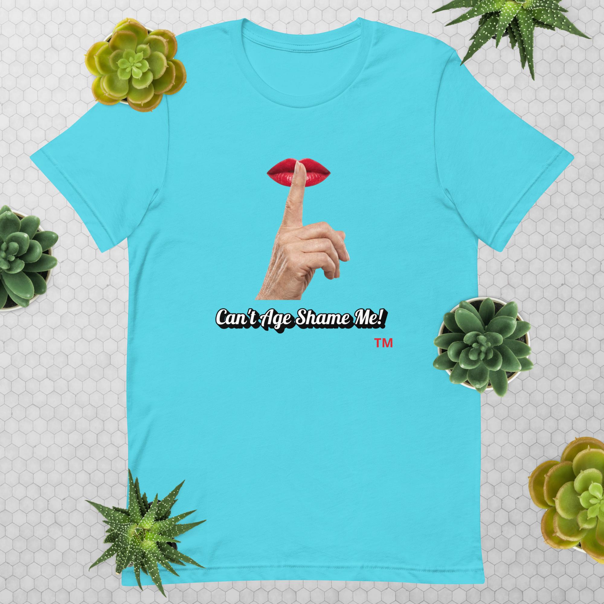 Turquoise t-shirt with graphic design of finger on mouth and text 'CAN'T AGE SHAME ME!' text logo on a light gray background with succulents.
