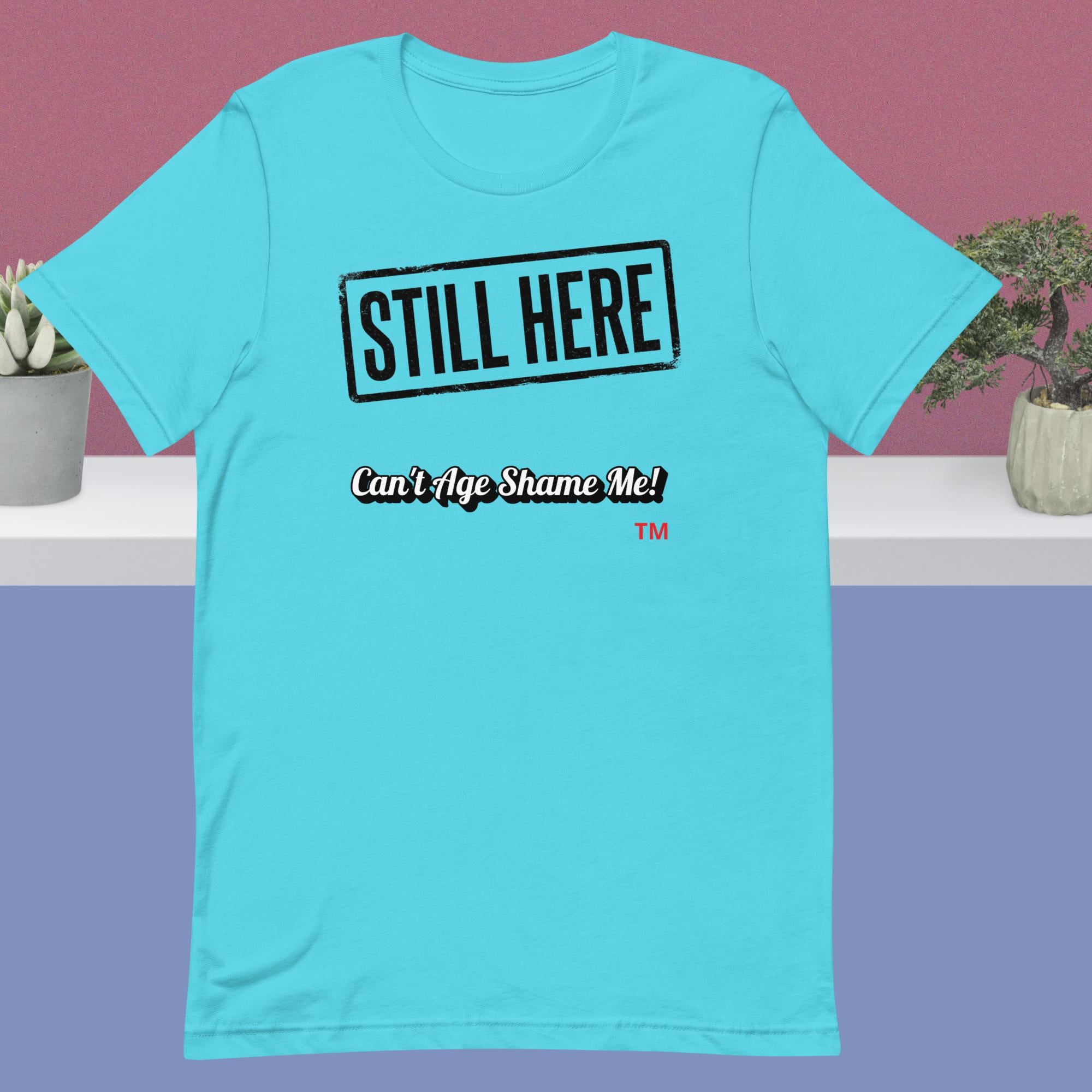 Blue t-shirt with 'STILL HERE Can't Age Shame Me!' text on a purple background