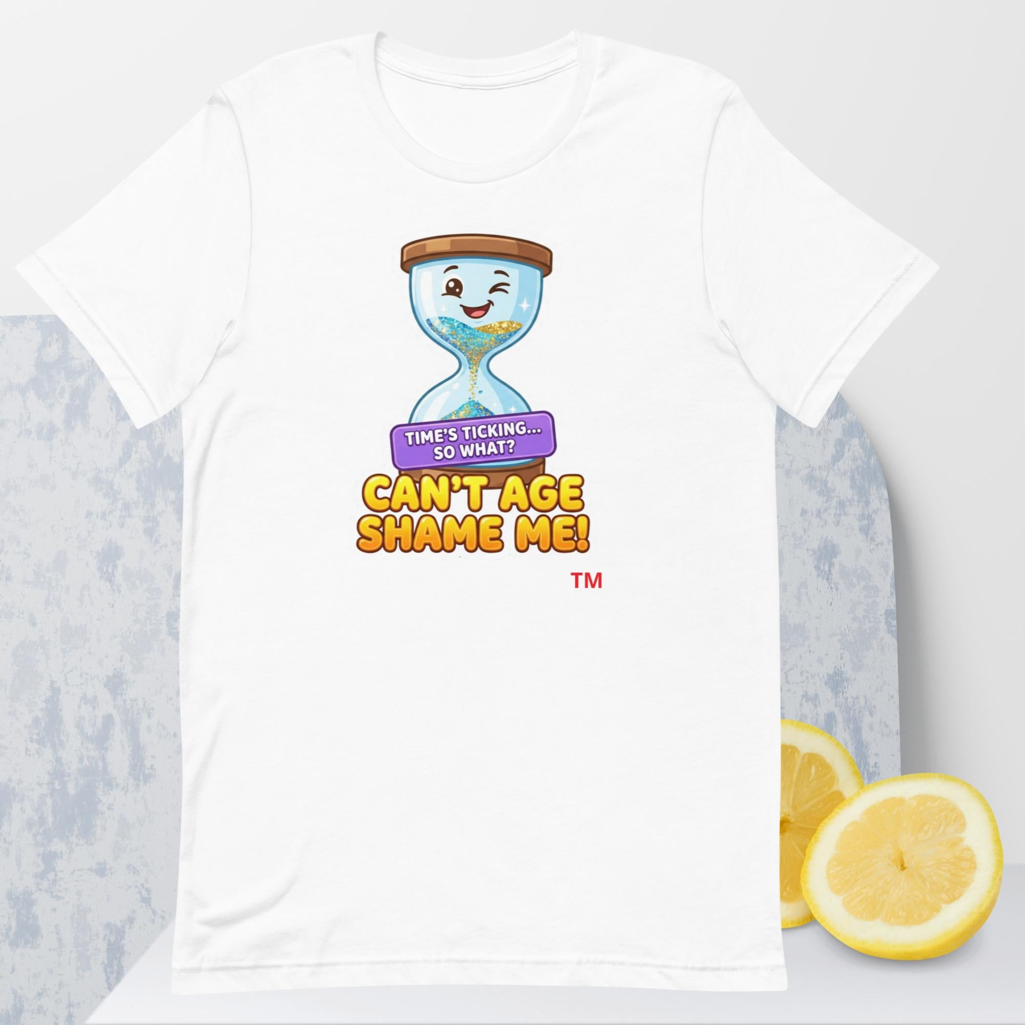 White t-shirt with a cartoon hourglass design and text 'Can't Age Shame Me' graphic on a light gray background.

