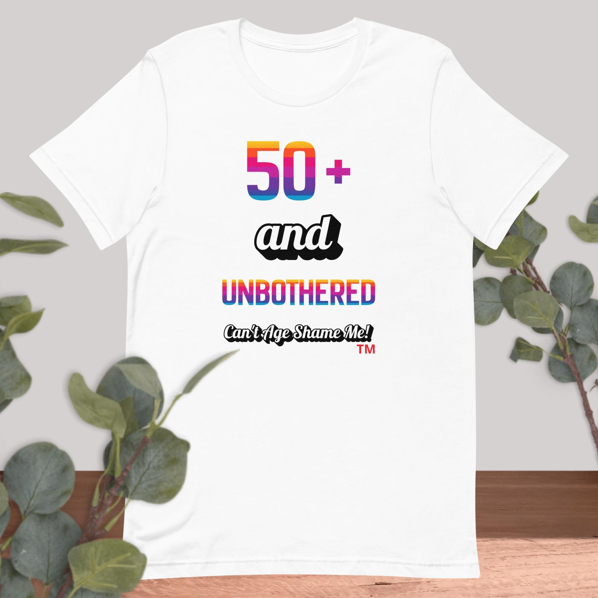 White t-shirt with colorful text design on a gray background with green leaves.