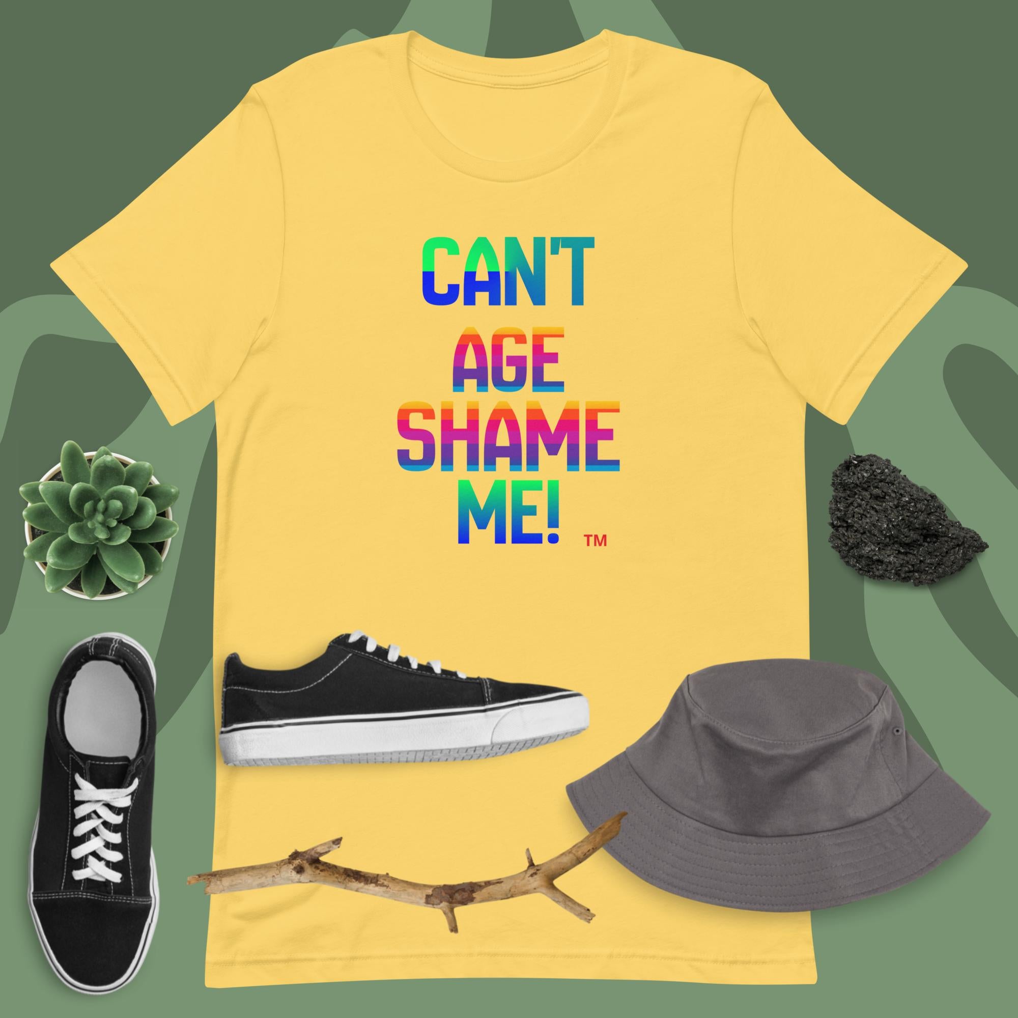 Yellow t-shirt with colorful text, black sneakers, gray bucket hat, and branch on a green background