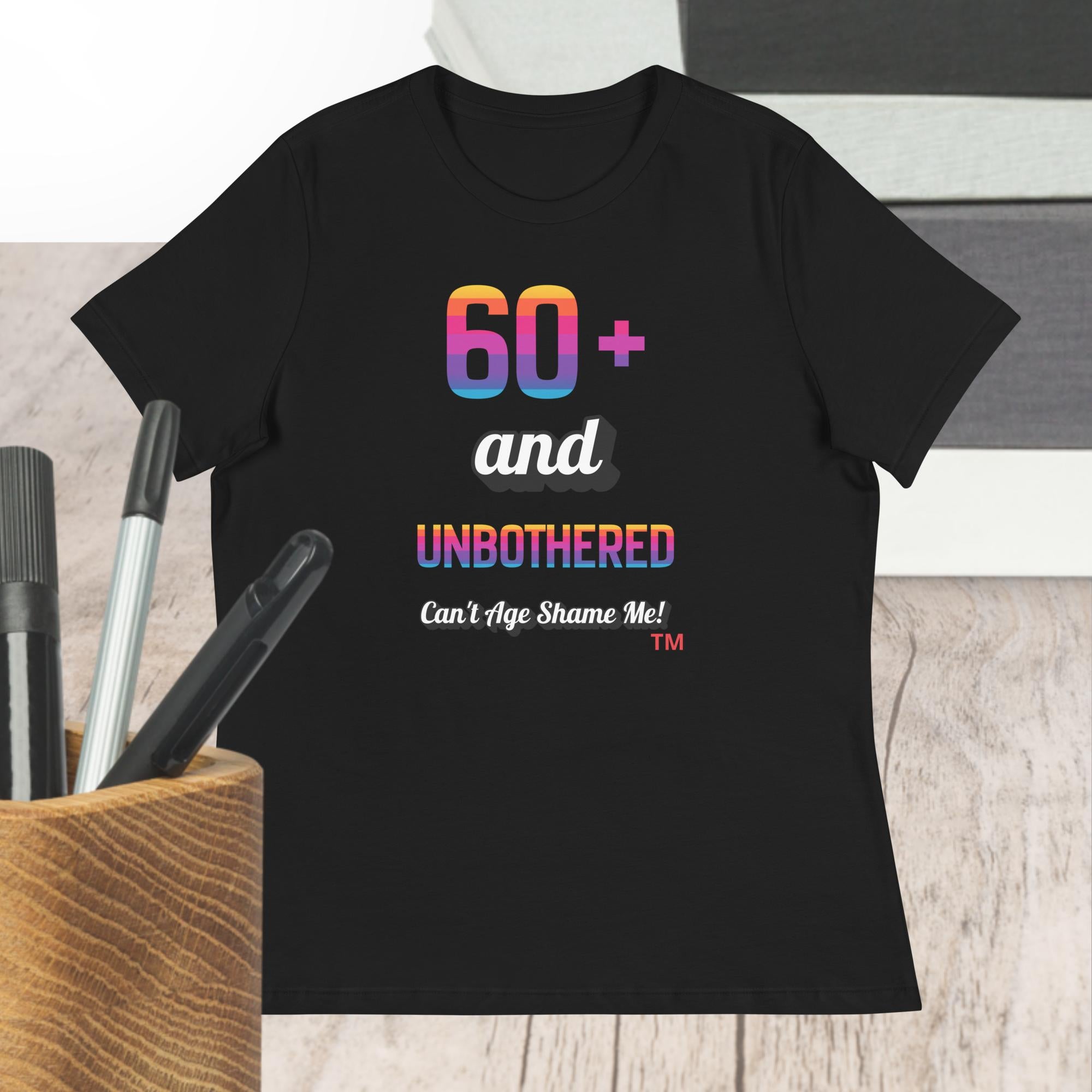 Black t-shirt with colorful text design on a wooden surface with pens.