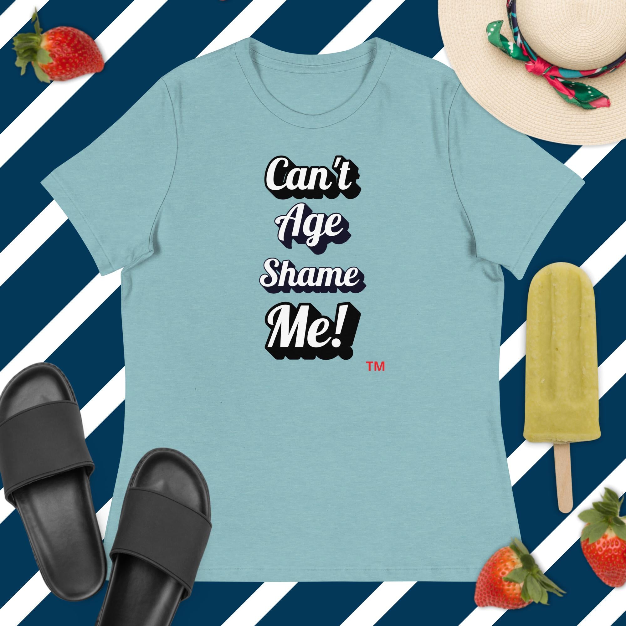 Light blue t-shirt with 'Can't Age Shame Me!' text, surrounded by black slides, a straw hat, and strawberries on a striped background.