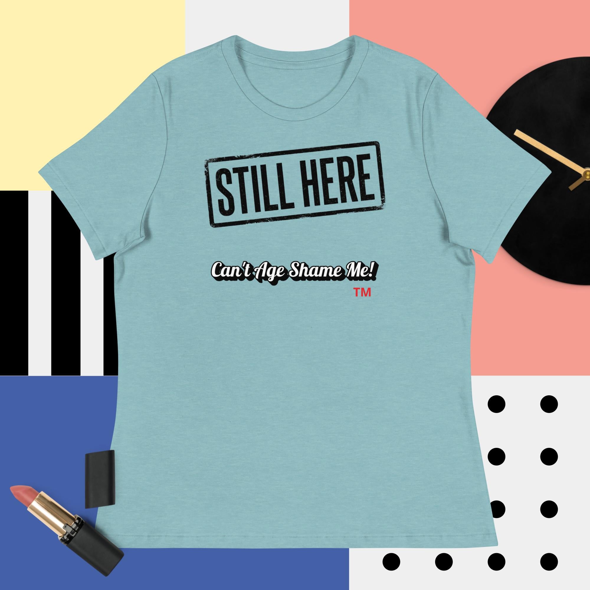 Light blue t-shirt with 'STILL HERE Can't Age Shame Me!' text on a colorful geometric background.