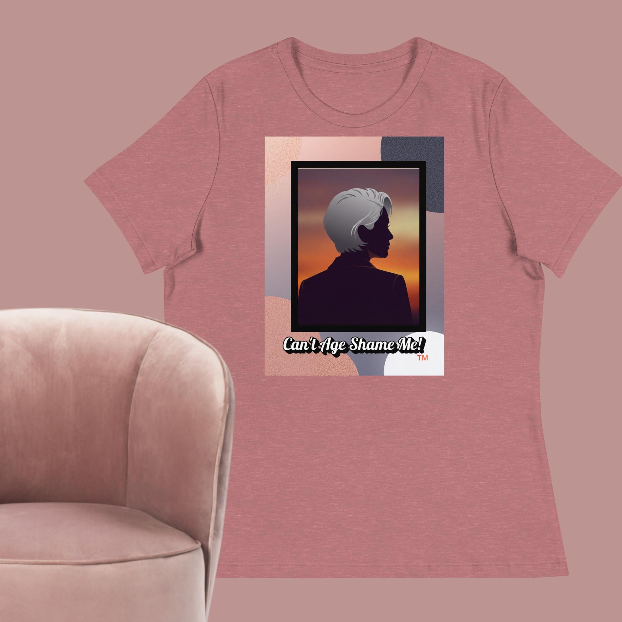 Mauve T-shirt with a graphic design featuring a woman with gray hair silhouette and text: Can’t Age Shame Me! surrounded by a pink chair against a pink background.

