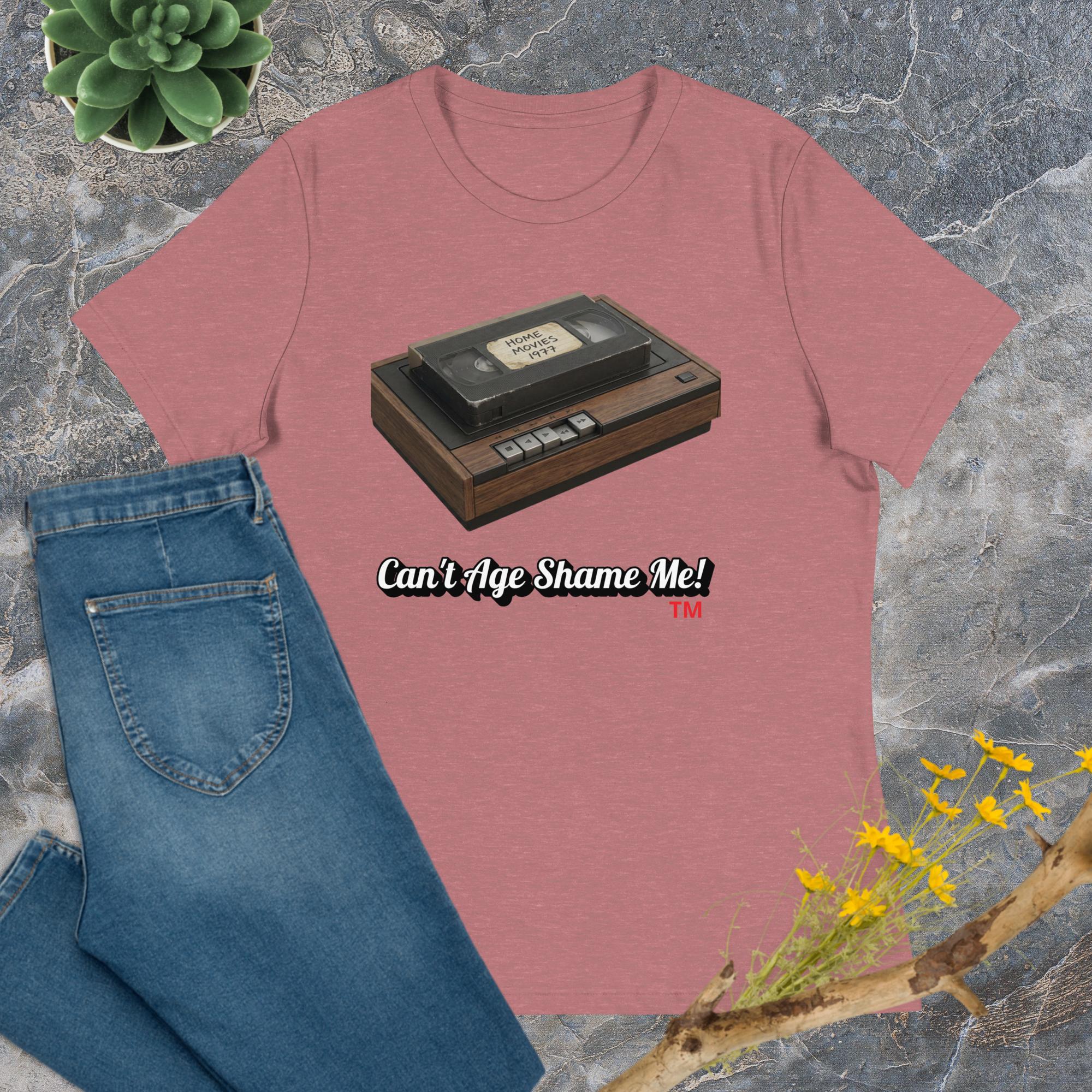 heather mauve t-shirt with a cassette tape graphic and 'Can't Age Shame Me!' text, paired with blue jeans on a textured surface.