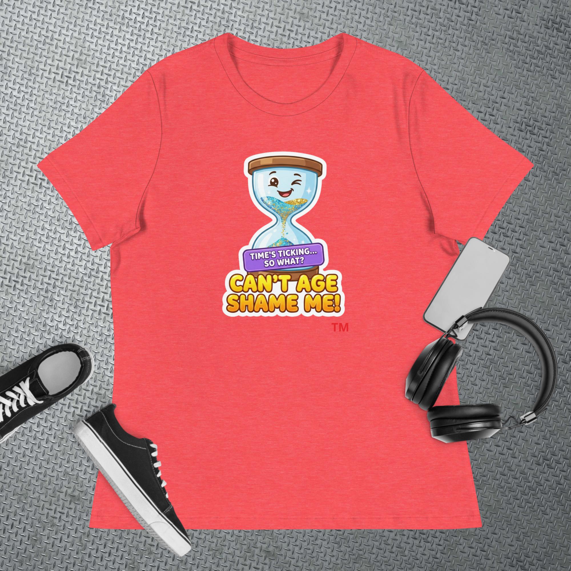 Heather Red  t-shirt with a cartoon hourglass graphic design and text 'Can't Age Shame Me' graphic on a textured gray surface with a sneaker and headphones
