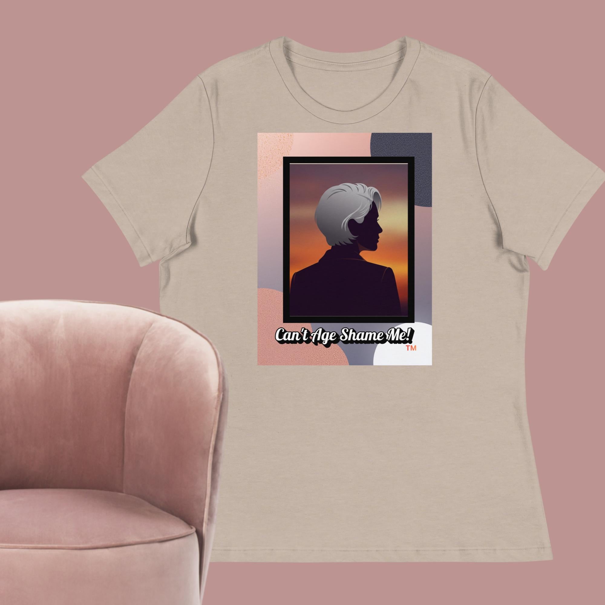 Beige Gray T-shirt with a graphic design featuring a woman with gray hair silhouette and text: Can’t Age Shame Me! surrounded by a pink chair against a pink background.

