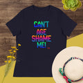 Black t-shirt with colorful text 'CAN'T AGE SHAME ME!' on a wooden surface with flowers and a hat.