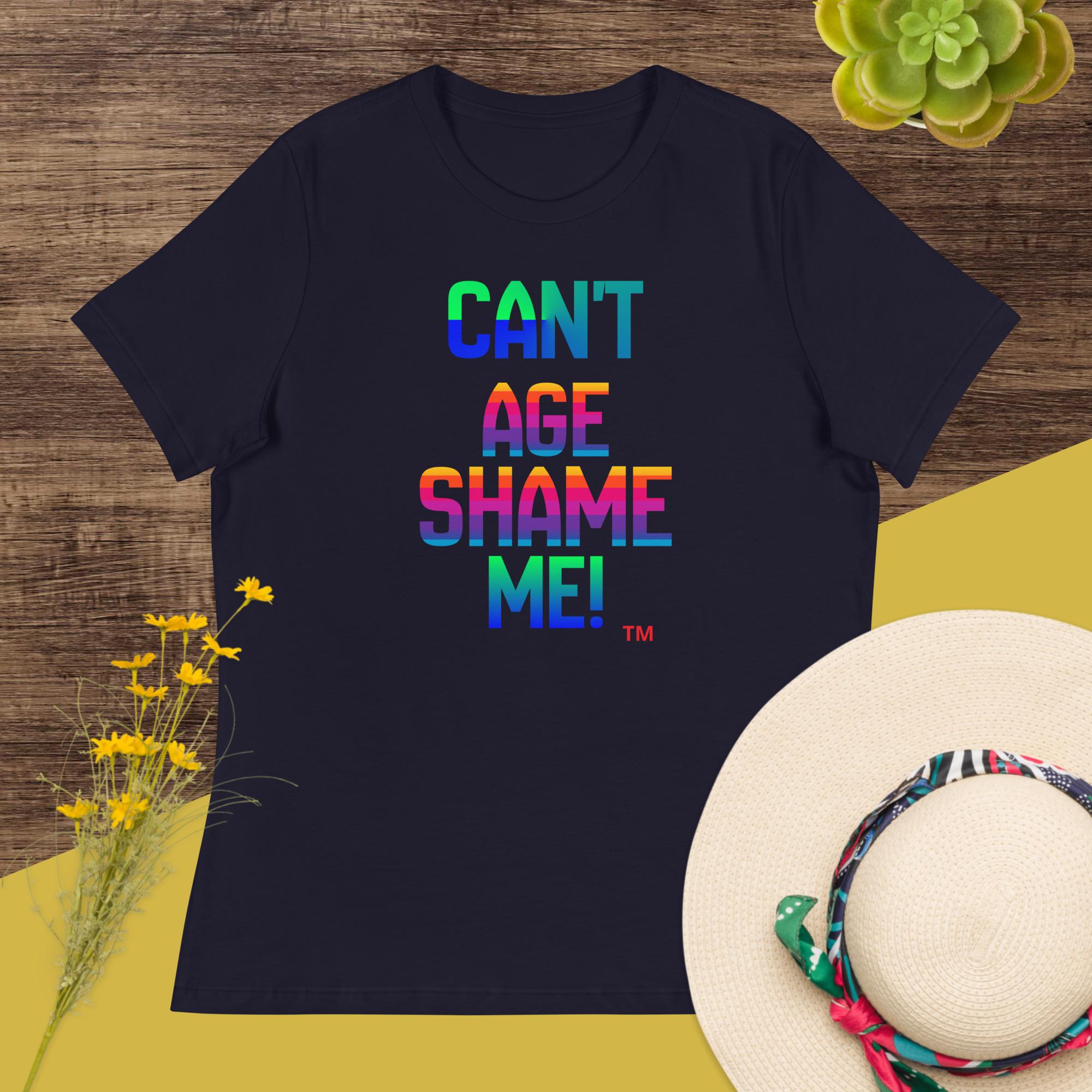 Black t-shirt with colorful text 'CAN'T AGE SHAME ME!' on a wooden surface with flowers and a hat.