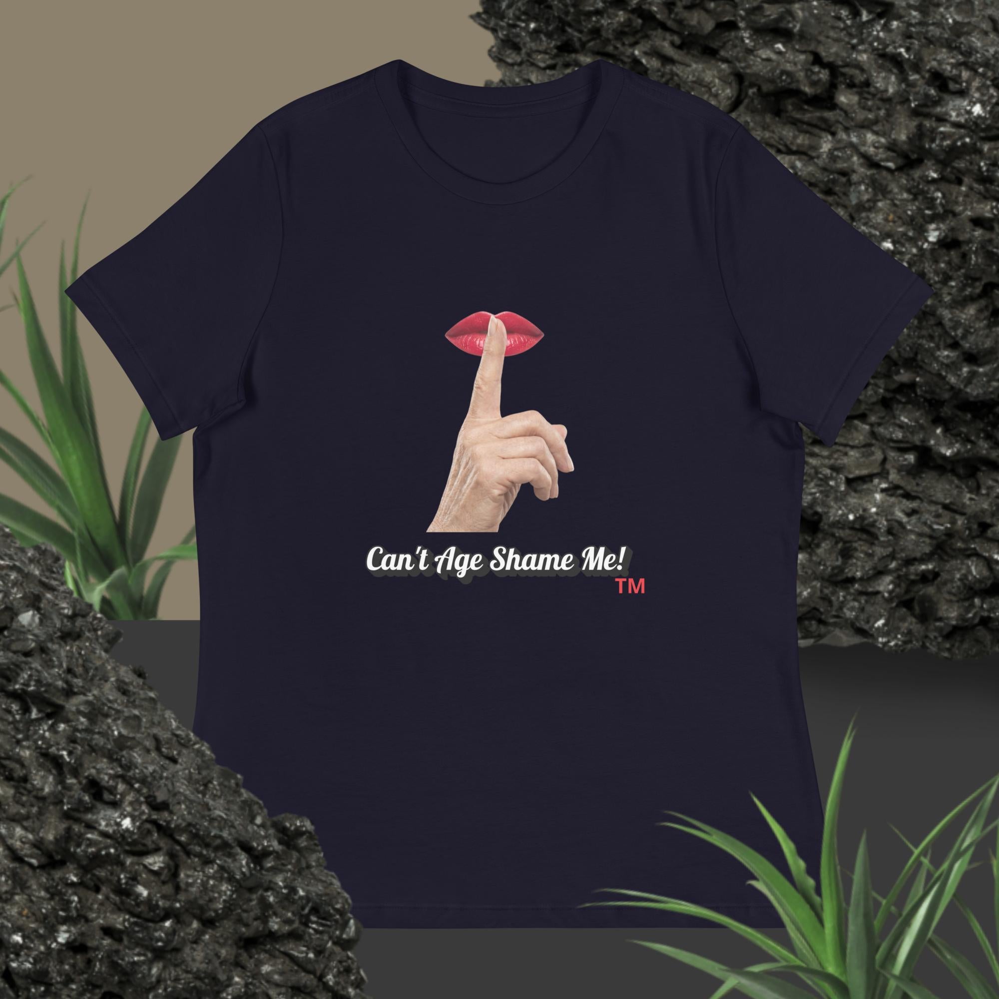Navy t-shirt with graphic design of finger on mouth and text 'Can't Age Shame Me' on a textured surface with plants.
