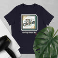 Navy  t-shirt with 'Still Confident! Can't Age Shame Me' graphic on a gray background with a plant and hair dryer.