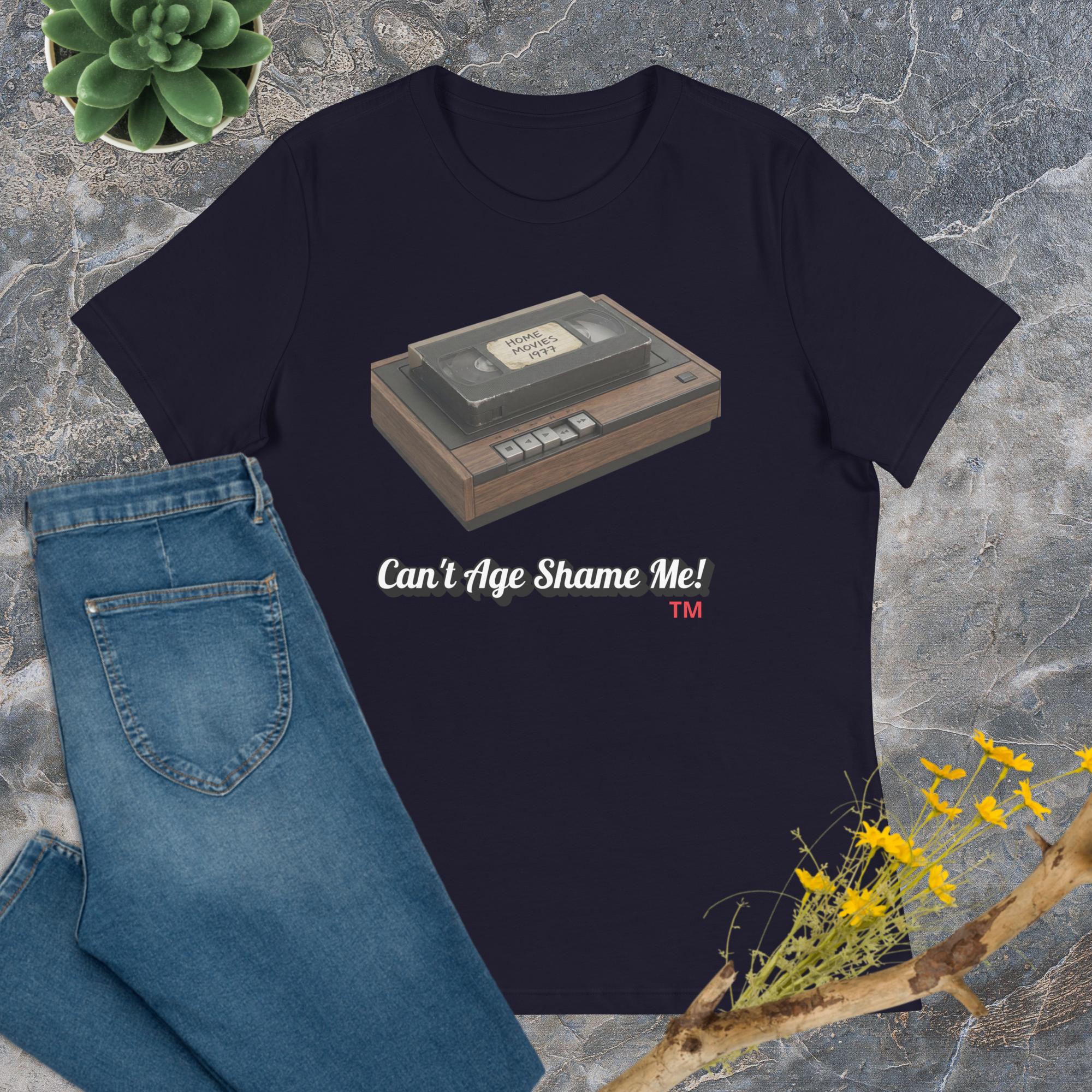 navy t-shirt with a cassette tape graphic and text 'Can't Age Shame Me!' on a stone surface with jeans and plants.