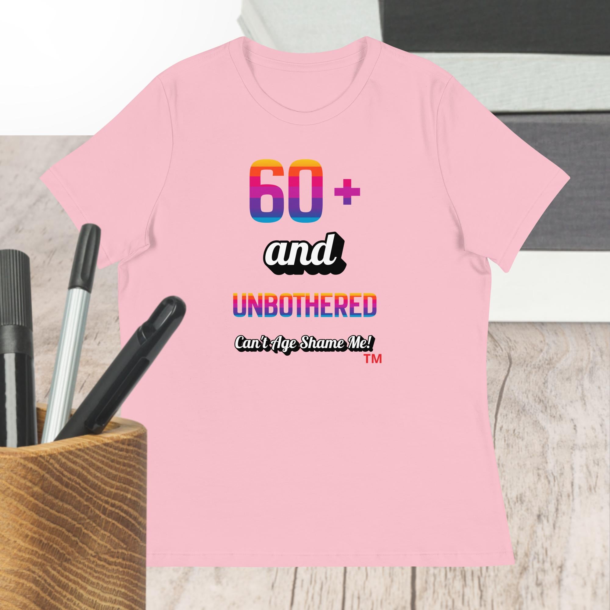 Pink t-shirt with colorful text design on a wooden surface with pens.