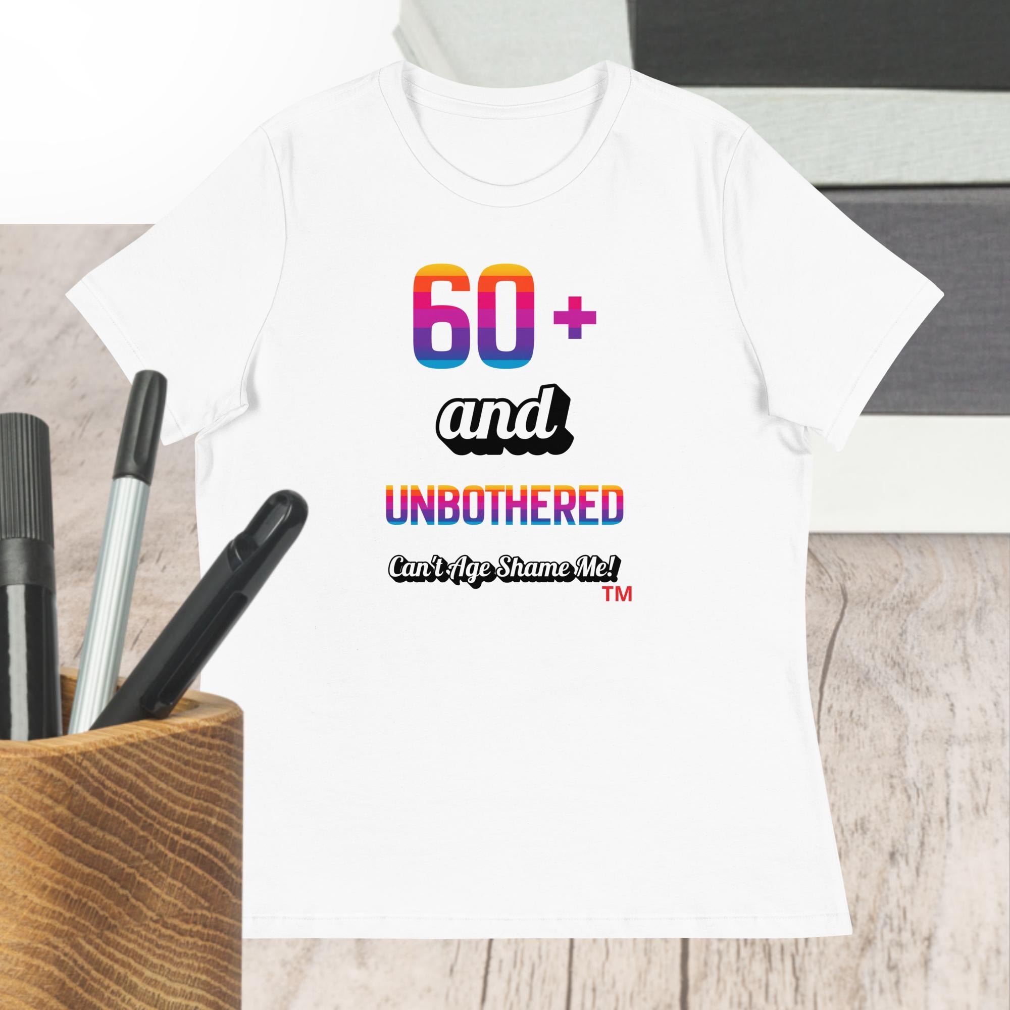 White t-shirt with colorful text design on a wooden surface with pens.