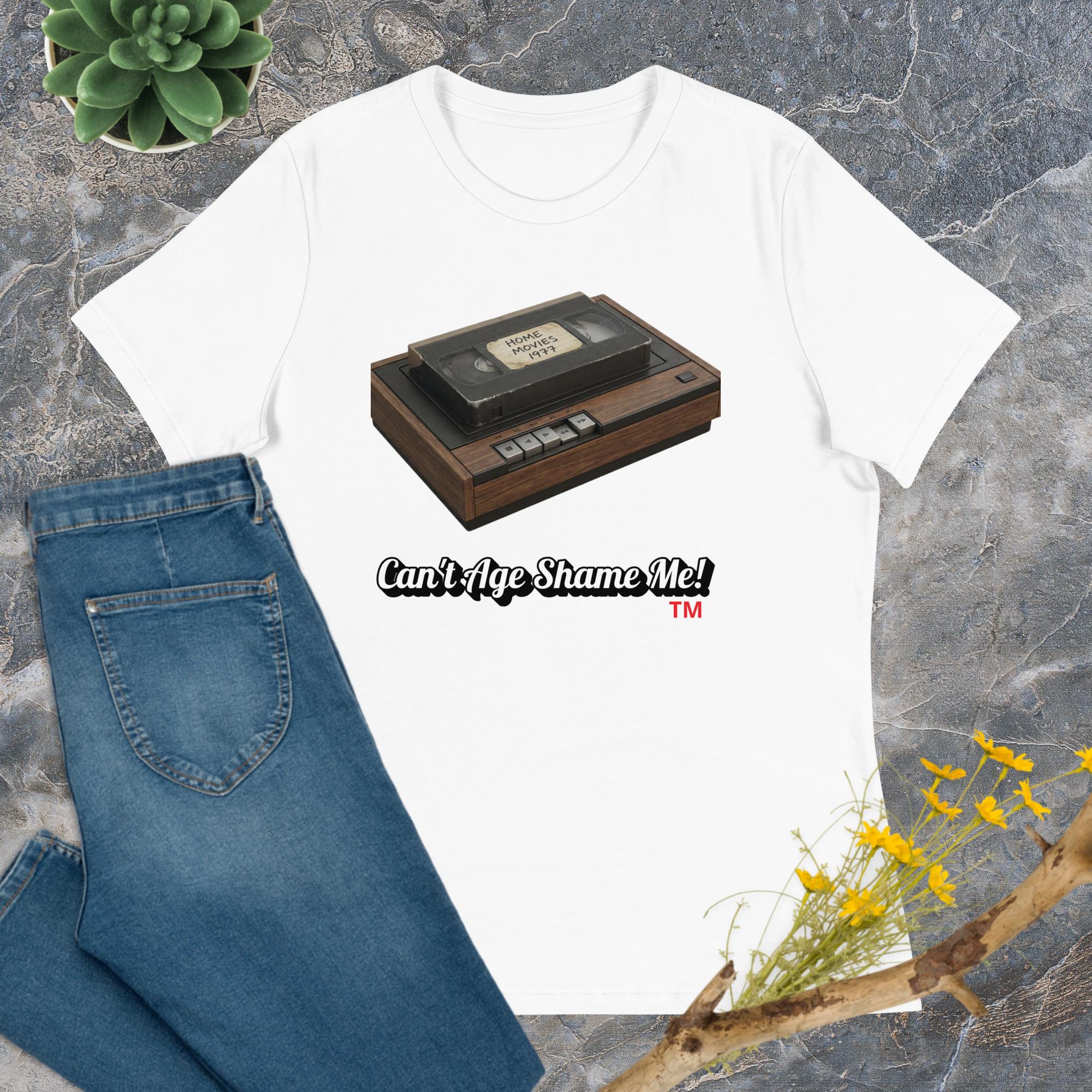 white t-shirt with a cassette tape graphic and text 'Can't Age Shame Me!' on a textured surface with jeans and plants.